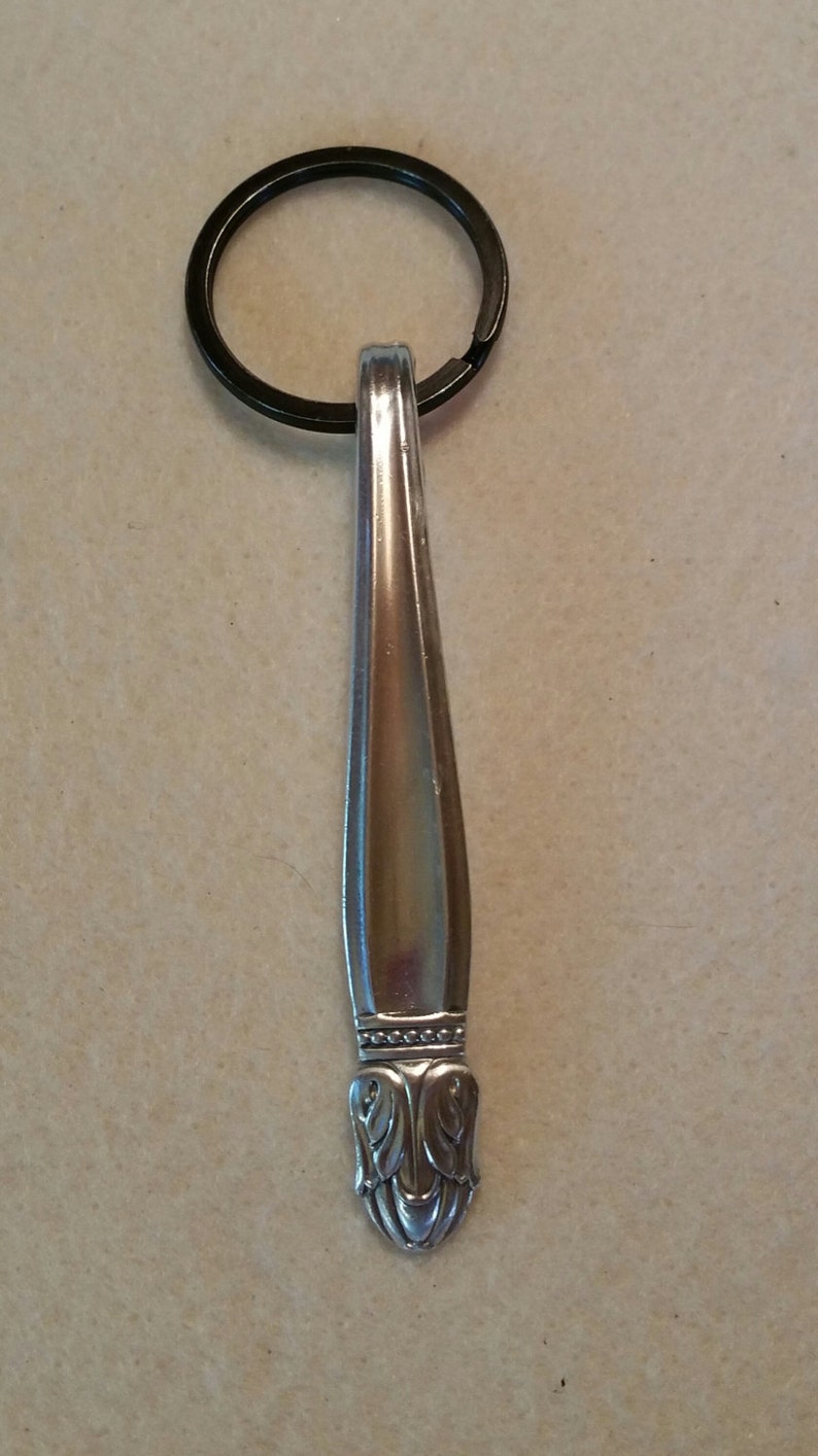 May include: A silver spoon keychain with a decorative handle and a black metal key ring.