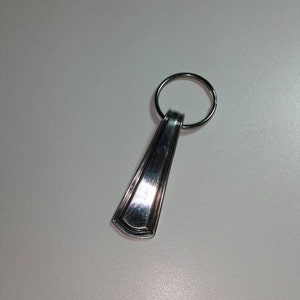May include: A silver key chain with a decorative spoon-shaped charm. The charm has a rounded top and a slightly pointed bottom.