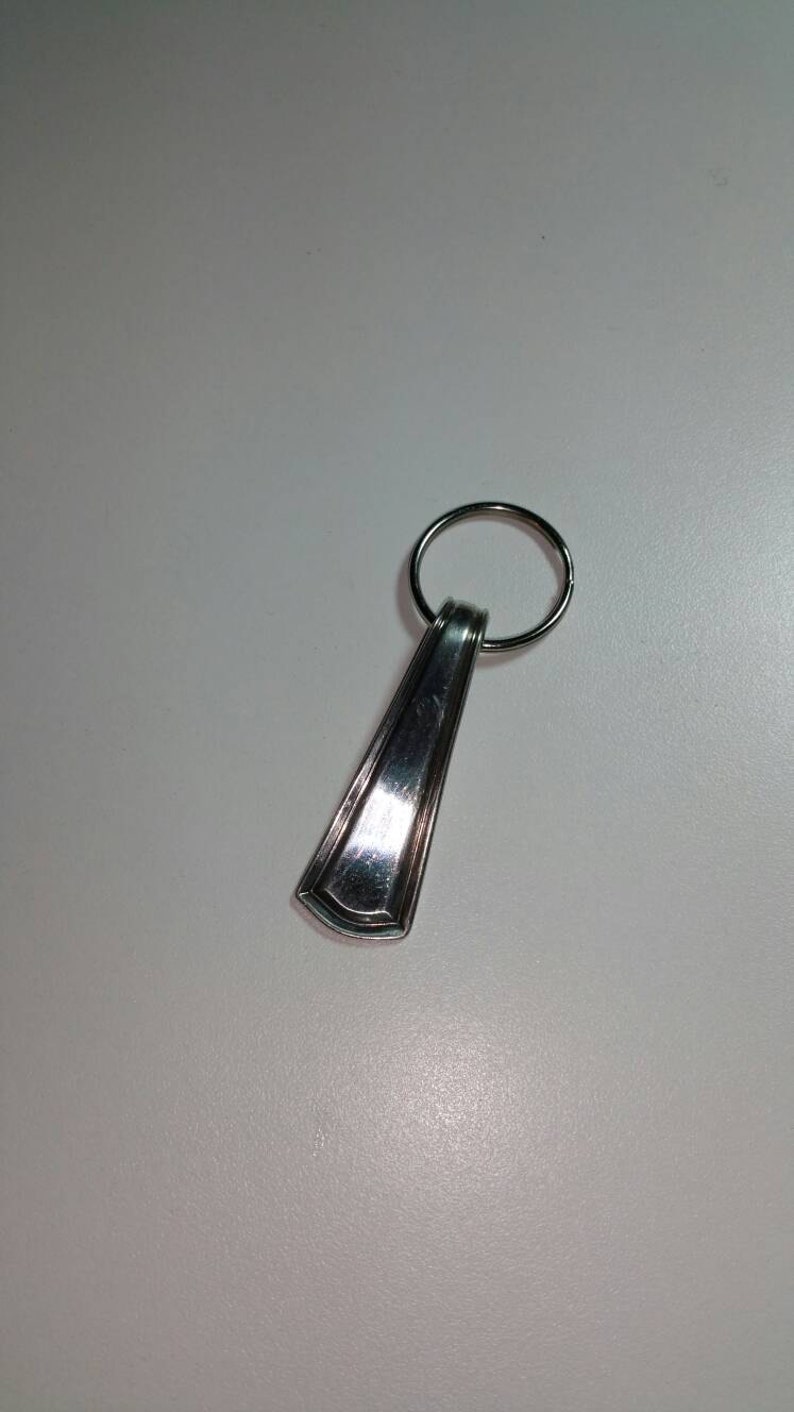 May include: A silver key chain with a decorative spoon-shaped charm. The charm has a rounded top and a slightly pointed bottom.
