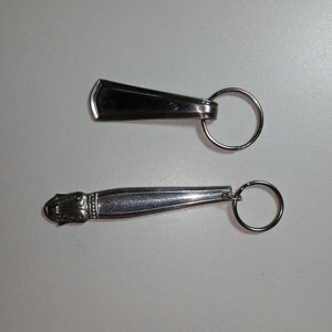 May include: Two silver keychains. The top keychain is a simple silver rectangle with a ring. The bottom keychain is a silver spoon with a decorative handle and a ring.