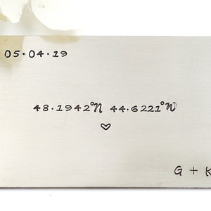 May include: A silver metal card with the date 05.04.19, coordinates 48.1942°N 44.6221°W, a heart symbol, and the initials G + K.