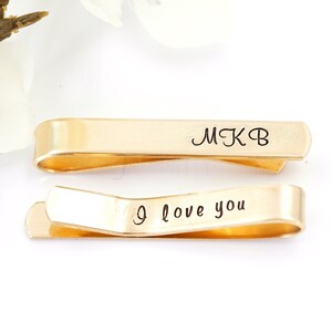 May include: Two gold tie clips with engraved text. The top clip says "MKB" and the bottom clip says "I love you".