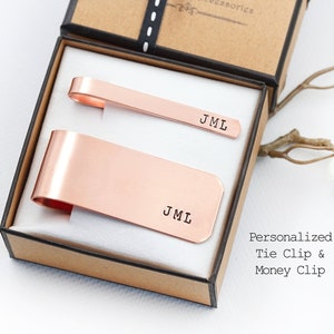 May include: A set of personalised copper tie clip and money clip in a brown box. The tie clip and money clip are engraved with the initials "JML".