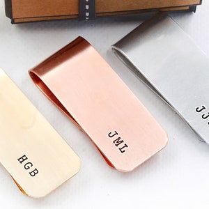 May include: Three personalized metal money clips in gold, rose gold, and silver. The clips are engraved with the initials "HGB", "JML", and "JJM".