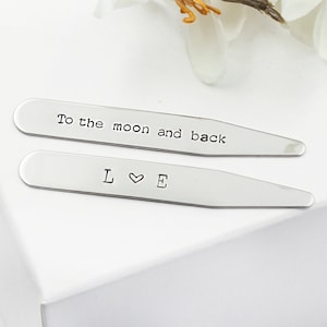 Op de afbeelding: Twee zilveren kraagstangen met gegraveerde tekst. De bovenste kraagstang luidt "To the moon and back". De onderste kraagstang luidt "L &hearts; E".
