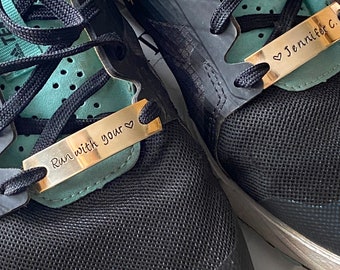 May include: Black running shoes with a gold metal tag that says "Run with your heart" on one shoe and a gold metal tag that says "Jennifer C." on the other shoe.