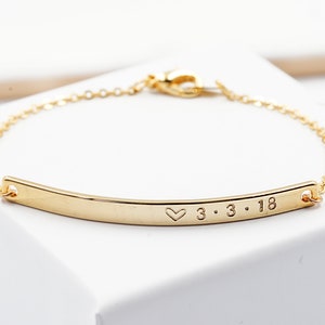 May include: Gold chain bracelet with a thin, curved bar charm engraved with a heart and the date 3.3.18.