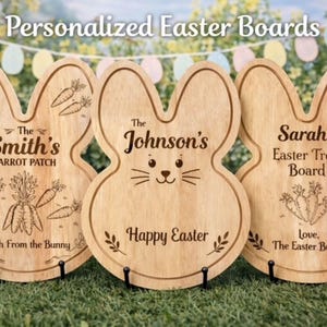 May include: Three wooden Easter bunny-shaped boards with personalized text and carrot illustrations. The boards are light brown and stand on black metal stands. Text includes "The Smith's Carrot Patch", "The Johnson's Happy Easter", and "Sarah's Easter Treat Board".