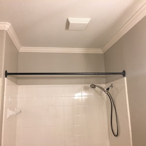 May include: A black shower curtain rod is installed above a white tiled shower stall. A silver shower head is attached to a hose and hangs down from the rod.