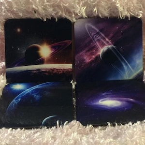 Peut inclure: Ensemble de quatre sous-verres carrés sur le thème de l'espace. Chaque sous-verre présente une image différente d'une galaxie, de planètes et d'étoiles dans des tons de bleu, de violet et de blanc.