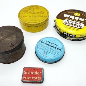 May include: Assortment of vintage tins, including a yellow tin labeled "Propert's Leather Soap", a brown tin labeled "Wren's Waterproofing Brown Dubbin", a blue tin labeled "Stuarts Micrometer Engineers Marking", and a red tin labeled "Five Schrader Valve Cores".