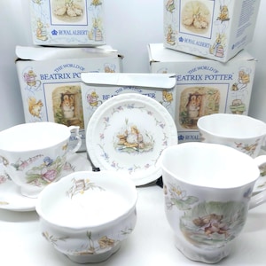 May include: A collection of Royal Albert Beatrix Potter fine bone china. The set includes teacups, saucers, bowls, and a plate, all featuring illustrations of Beatrix Potter characters. The items are displayed with their original boxes, showcasing the "Beatrix Potter" and "Royal Albert" branding.