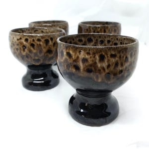 May include: A set of four ceramic goblets. The bowls feature a speckled brown pattern over a dark brown base. The stems are glossy black. The goblets are set against a white background.