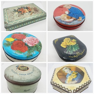 May include: A selection of vintage decorative tins. Features a rectangular tin with a floral design, a round tin with a child and cat, a blue tin with roses, a black tin with yellow roses, a cylindrical tin with text, and a hexagonal tin with a portrait.
