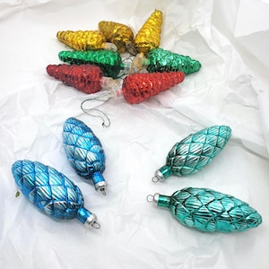 May include: A selection of vintage Christmas tree ornaments in the shape of pine cones. The ornaments are in gold, green, red, blue, and teal. They have a textured surface and silver metal caps.