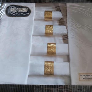 May include: A boxed cotton damask table set. The set includes a white tablecloth with a leaf pattern, four rolled napkins, and gold napkin rings. The box has the "Old Mill" logo.