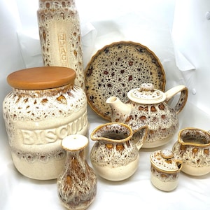 May include: A collection of vintage ceramic kitchenware with a speckled brown and cream glaze. Includes a biscuit jar, a canister labeled "SPACE", a teapot, a plate, a creamer, a sugar bowl, and small vases.