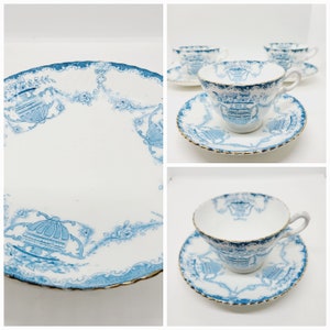 May include: A set of three blue and white teacups and saucers with a gold trim. The cups and saucers feature a delicate floral pattern with a central design of a dome-shaped structure.