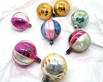 May include: A collection of vintage Christmas ornaments in various colors. The ornaments include gold, silver, pink, blue, and green. Some have painted designs, while others are solid. The ornaments are round and have metal caps for hanging.