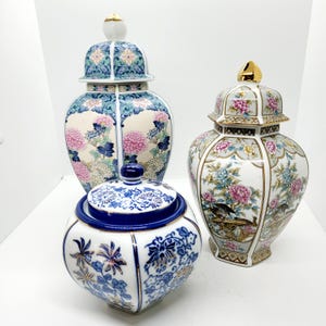 Könnte beinhalten: Drei Porzellanvasen mit Blumendesigns. Die größte Vase ist blau und weiß mit rosa Blumen. Die mittlere Vase ist weiß mit rosa und blauen Blumen. Die kleinste Vase ist blau und weiß mit goldenen Akzenten.
