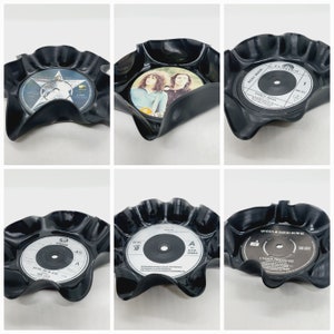 May include: Six black vinyl record coasters with different album covers. The coasters are shaped like a flower with a ruffled edge. The album covers include "Dance Away" by Roxy Music, "Under Pressure" by Queen and David Bowie, "Another Time, Another Place" by The Cure, "Queen" by Queen, and two others.