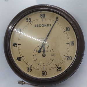 May include: A brown, round, analog clock with a white face and black markings. The clock has two hands, one for seconds and one for minutes. The clock face reads "SECONDS" and "MINUTES". The clock is made in England.