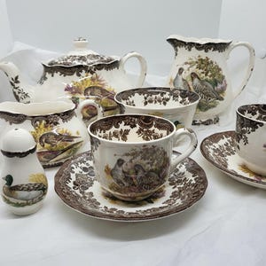 May include: A brown and white tea set with a bird and floral pattern. The set includes a teapot, creamer, sugar bowl, two teacups and saucers, and a jug.