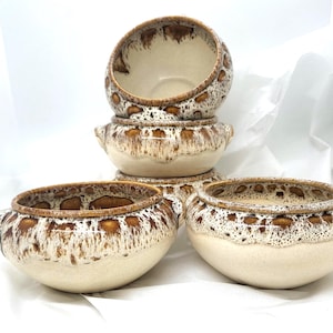 May include: A collection of five ceramic bowls, featuring a speckled brown and cream glaze. The bowls have a rounded form with small handles. The interior of the bowls is a plain cream colour.