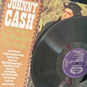 May include: A Johnny Cash vinyl record and its album cover titled I Forgot To Remember To Forget. The cover features a portrait of Johnny Cash in a black hat and a tracklist including I Love You Because, Train Of Love, and Home Of The Blues.