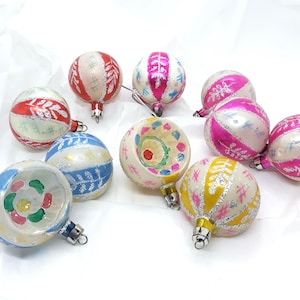 May include: A collection of vintage Christmas ornaments in various colors. The ornaments are round with silver caps and feature designs in red, pink, blue, and yellow. Some have stripes, while others have floral or geometric patterns.