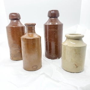 Peut inclure: Quatre bouteilles en grès vintage, deux brunes, une beige et une avec un dessus brun et un corps beige. Les bouteilles brunes ont du texte en relief, l'une indique "TRADE MARK" et l'autre "WOODS".