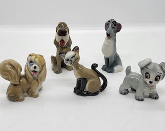 May include: A set of five ceramic animal figurines. The collection features a brown dog, a grey dog, a tan cat, a grey puppy, and a tan dog with a long tail. Each figurine is painted with detailed features and stands on its own.