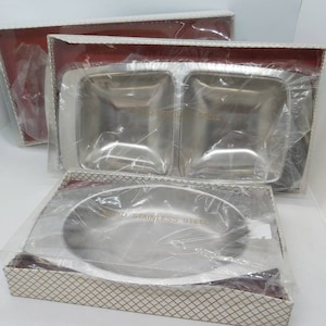 May include: Three silver serving dishes in their original packaging. The dishes are made of solid stainless steel and are packaged in white boxes with a gold and white checkered pattern.