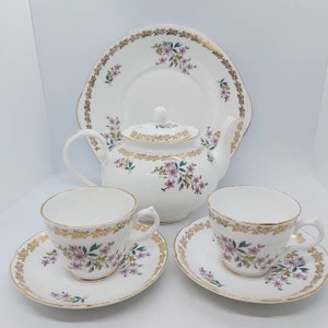 Könnte beinhalten: Ein weißes Teeservice mit floralem Muster und goldener Verzierung. Das Set beinhaltet eine Teekanne, zwei Tassen und zwei Untertassen.