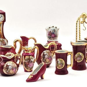 May include: A collection of miniature porcelain figurines in burgundy and gold. The set includes a clock, pitchers, a shoe, mugs, and a well, each adorned with a painted scene of people. The figurines are likely decorative items.
