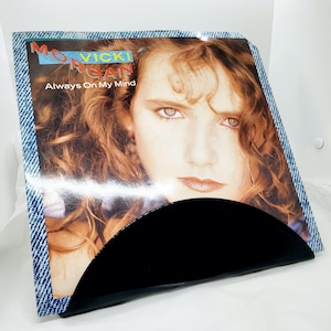 May include: A vinyl record album cover featuring a portrait of a woman with auburn hair. The album is titled "Always On My Mind" by Mo Vicki Morgan. The album cover is in a denim-patterned sleeve with a black, curved holder.