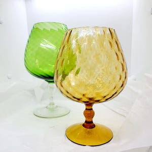 May include: Two vintage glass decanters, one green and one amber, with a textured, bubbled design. Both decanters have a round base and a tall, slender stem.