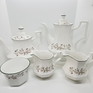 May include: A white tea set with a floral pattern. The set includes a teapot, creamer, sugar bowl, and two cups.