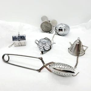 May include: A set of five silver tea infusers, including a teapot, a house, a ball, a cone, and a pair of tongs. The infusers are made of stainless steel and have a mesh design.