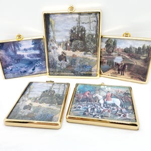 May include: Five framed pictures with gold frames and different landscape scenes. The pictures are hanging on a white wall.