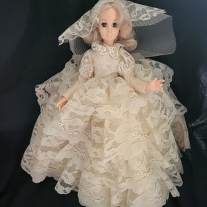 May include: A porcelain doll wearing a white lace wedding dress and veil. The doll has blonde hair and blue eyes.