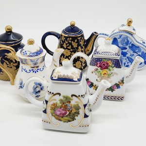 Könnte beinhalten: Eine Sammlung von sechs Miniatur-Porzellan-Teekannen mit aufwendigen floralen und geometrischen Designs. Die Teekannen sind mit goldenen Akzenten und blau-weißen Mustern verziert.