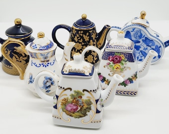 May include: A collection of six miniature porcelain teapots with intricate floral and geometric designs. The teapots are decorated with gold accents and blue and white patterns.