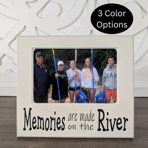 May include: White picture frame with a black inscription that reads "Memories are made on the River". The frame has a photo of a family of five standing in a forest with blue paddles in their hands.