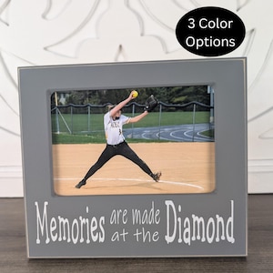 May include: A rectangular gray picture frame with white text that reads "Memories are made at the Diamond" printed on the bottom border. The frame contains a photograph of a softball player in a white uniform pitching on a dirt field.