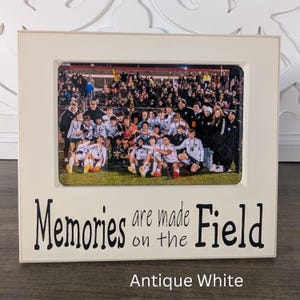 May include: White picture frame with a black inscription that reads "Memories are made on the field". The frame has a photo of a soccer team in their uniforms. The frame is labeled "Antique White".