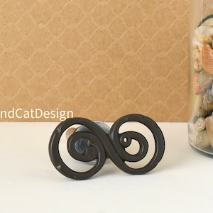 May include: A black metal cabinet knob with an intricate infinity symbol design.