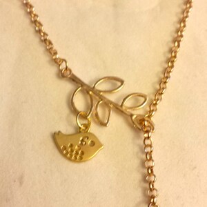 Puede incluir: Un collar de oro con un delicado diseño de rama y dos pequeños colgantes de pájaro. Los pájaros tienen un patrón de puntos y las letras "S" y "R" están grabadas en ellos.