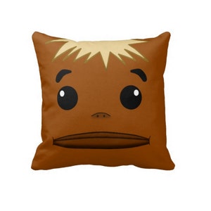 May include: A square decorative pillow featuring a cartoon face design. The pillow has a brown background with a face illustration. The face has large black eyes, a small nose, and a wide mouth. The hair is light brown.