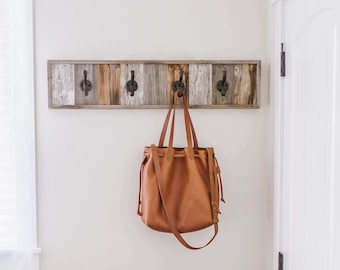 May include: A white rocking chair with a white pillow sits in a room with white walls and a white door. A brown leather bag hangs on a wooden rack on the wall.